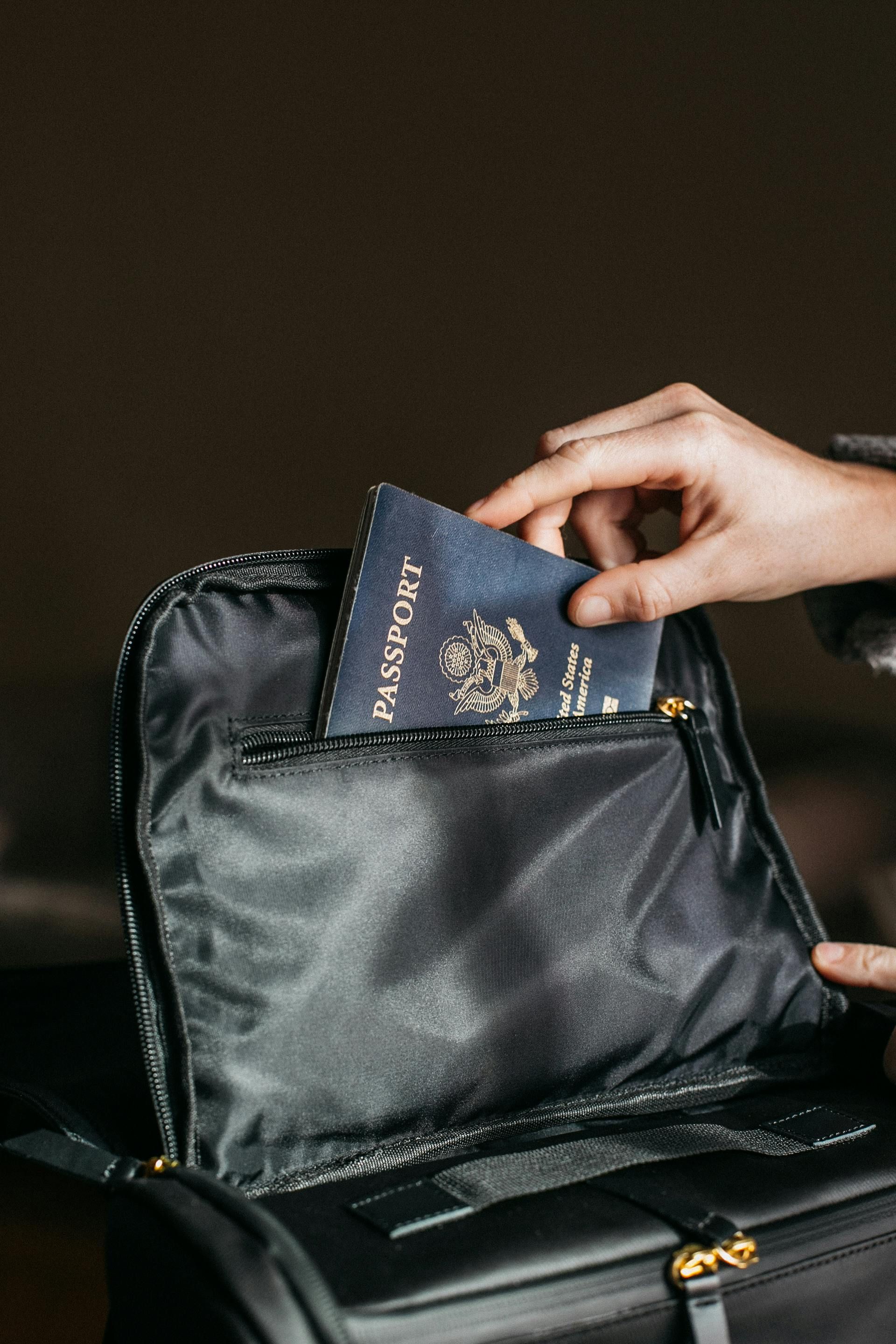 Hand putting a passport into a black backpack's zippered pocket.