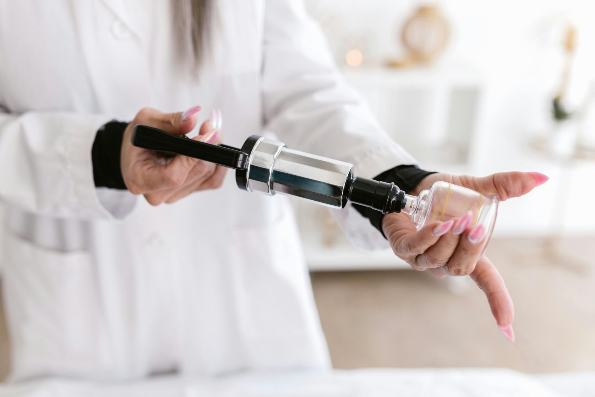 Person in lab coat using a suction device on a glass cup.