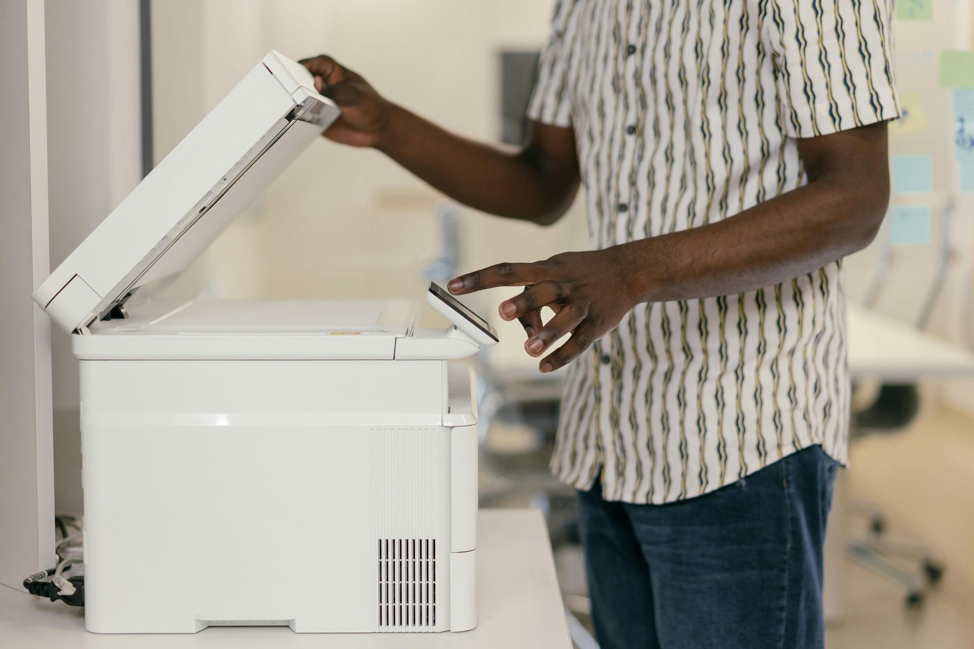 Person using a white printer. They lift the lid and press a button on the control panel.